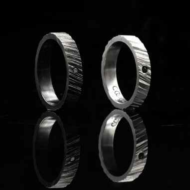 Photo des deux alliances homme avec diamant noir et blanc modèle tungstène sur fond marbre noir.